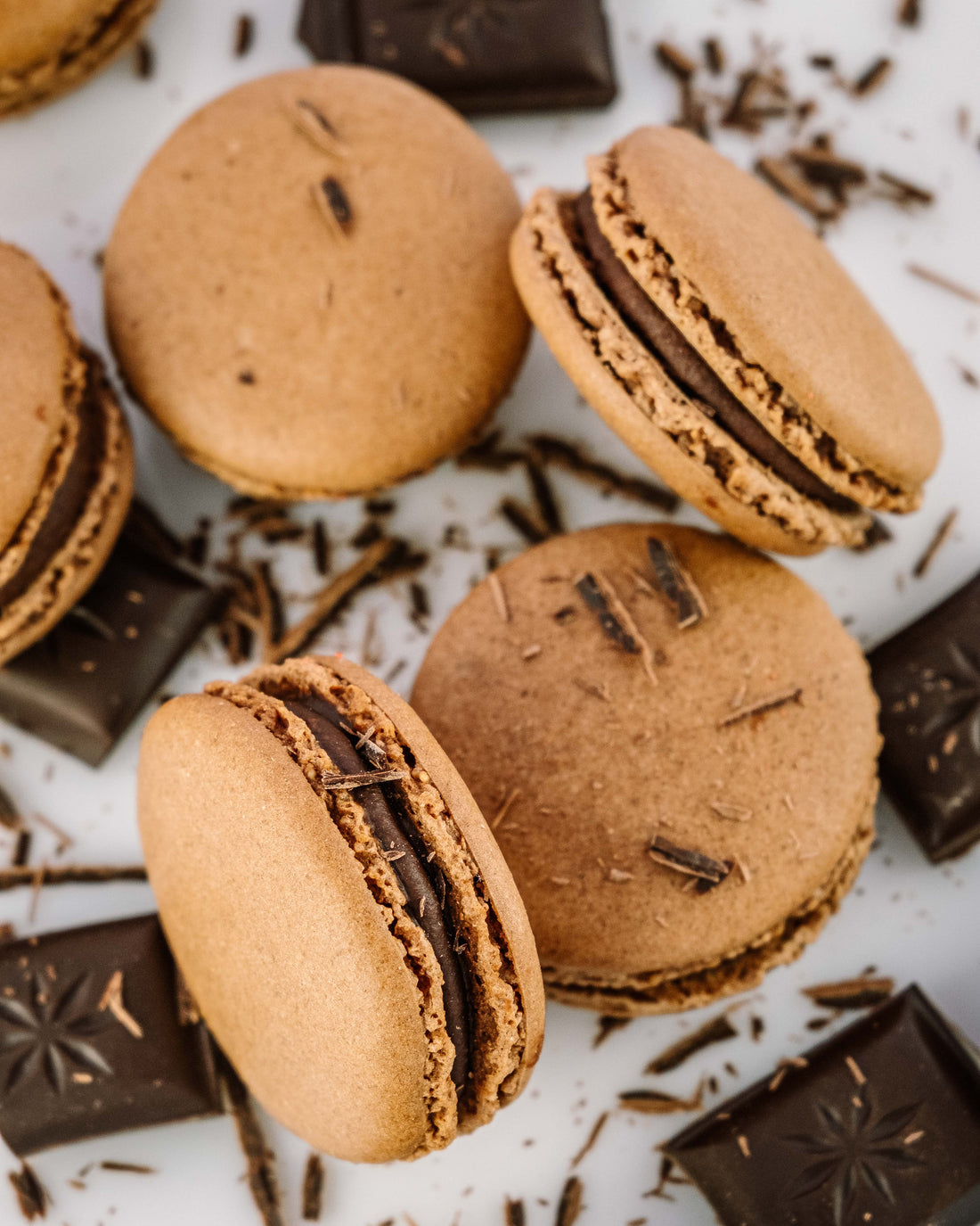 Five Dark chocolate macaroons by Miss Macaroon, surrounded by dark chocolate pieces and flakes of dark chocolate