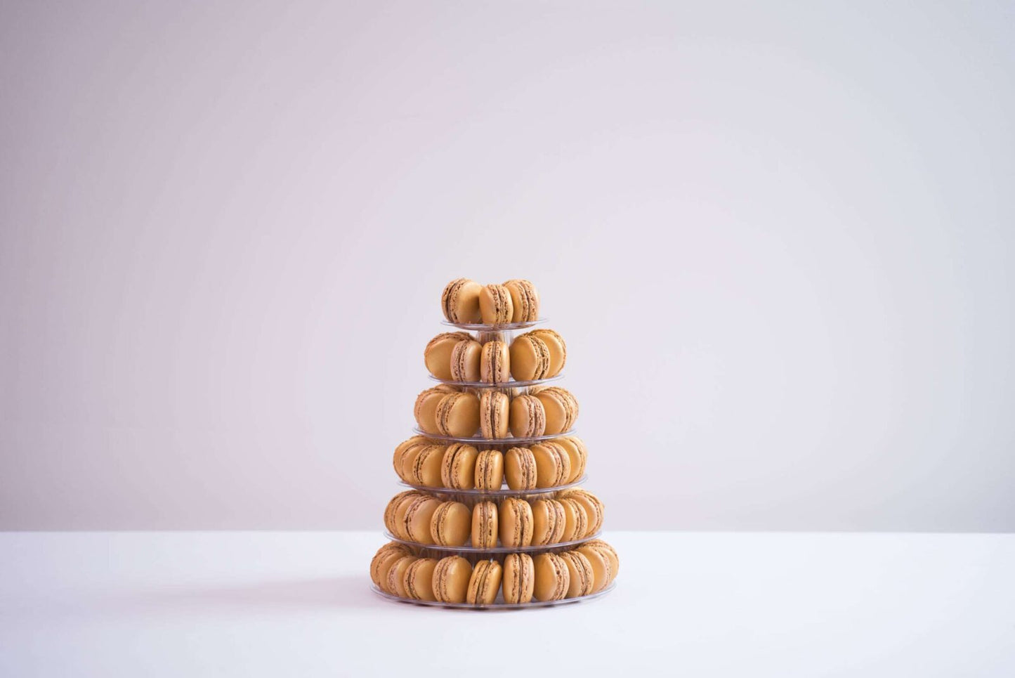 A tower of six tiers is placed in the center. The background is a plain white and the macaroons are shades of yellow and orange.