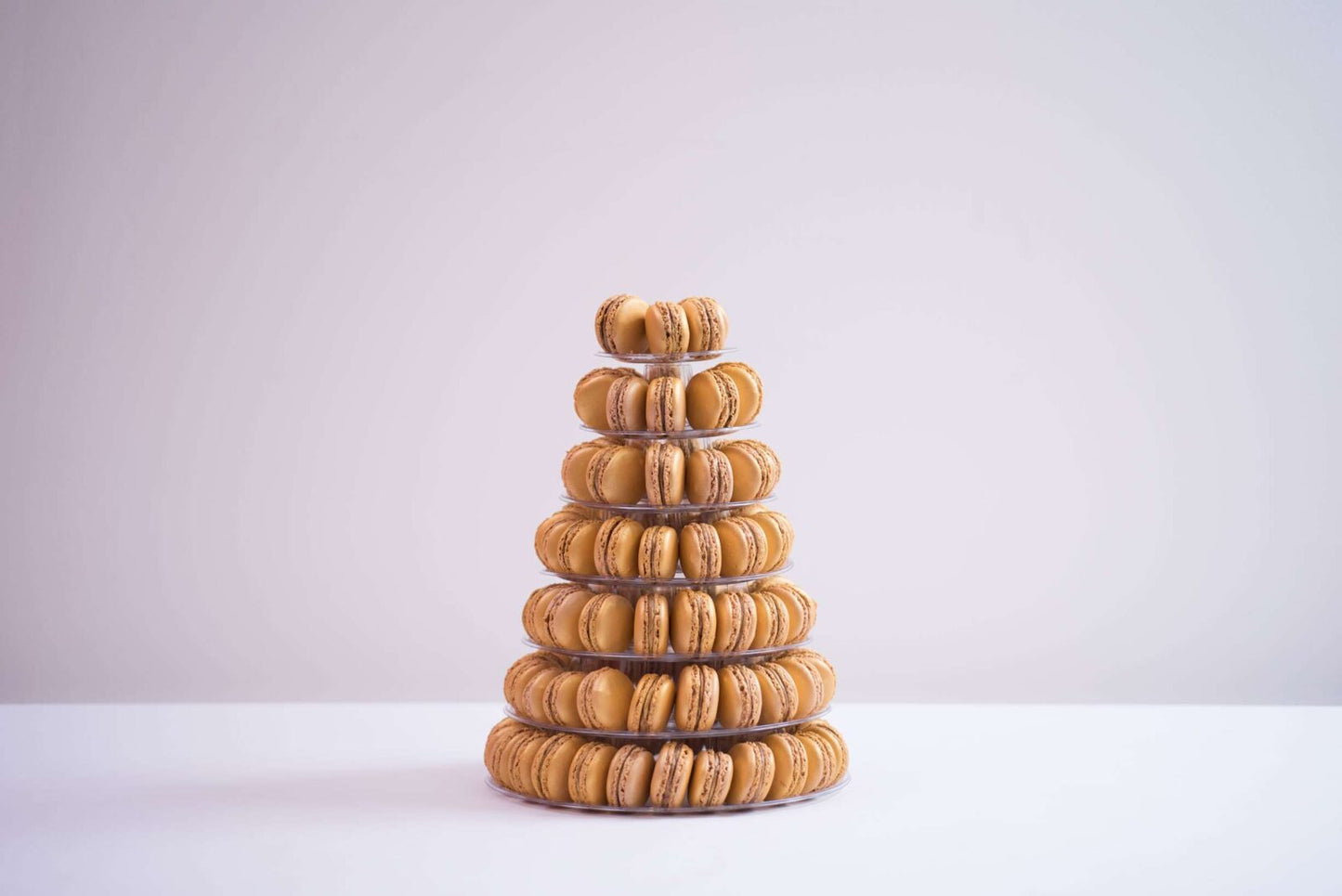 A tower of seven tiers is placed in the center. The background is a plain white and the macaroons are shades of yellow and orange.