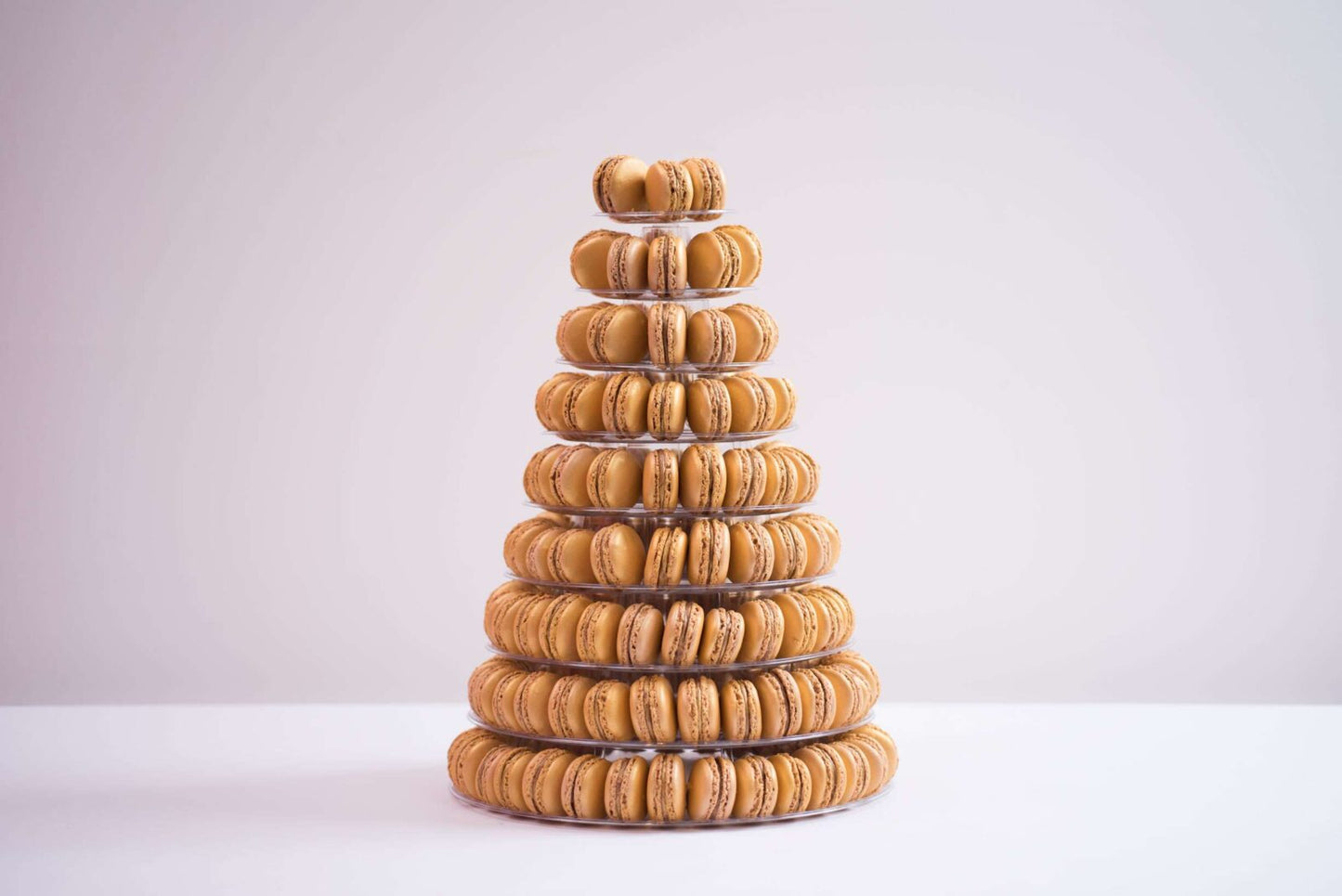 A tower of nine tiers is placed in the center. The background is a plain white and the macaroons are shades of yellow and orange.