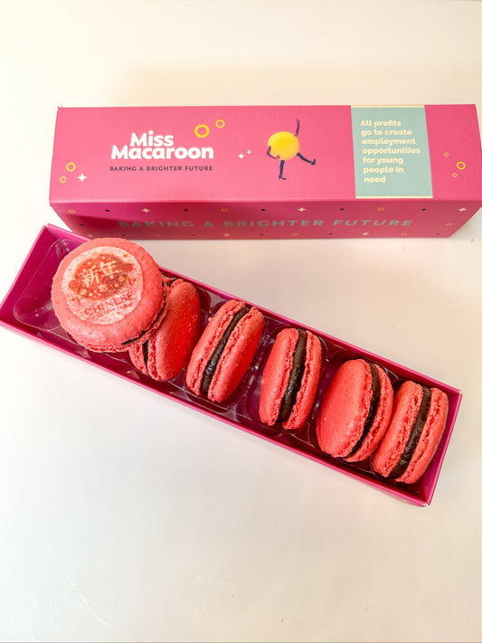 Box of red macarons with a pink 'Miss Macaron' box on a white background