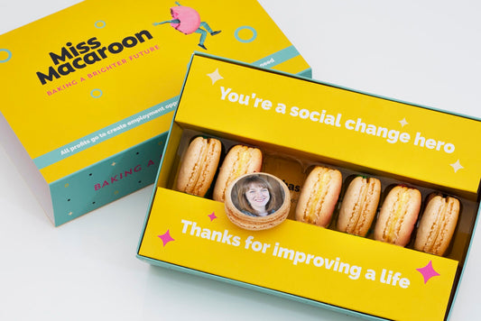 Yellow gift box of seven cream macaroons printed with a woman's face.