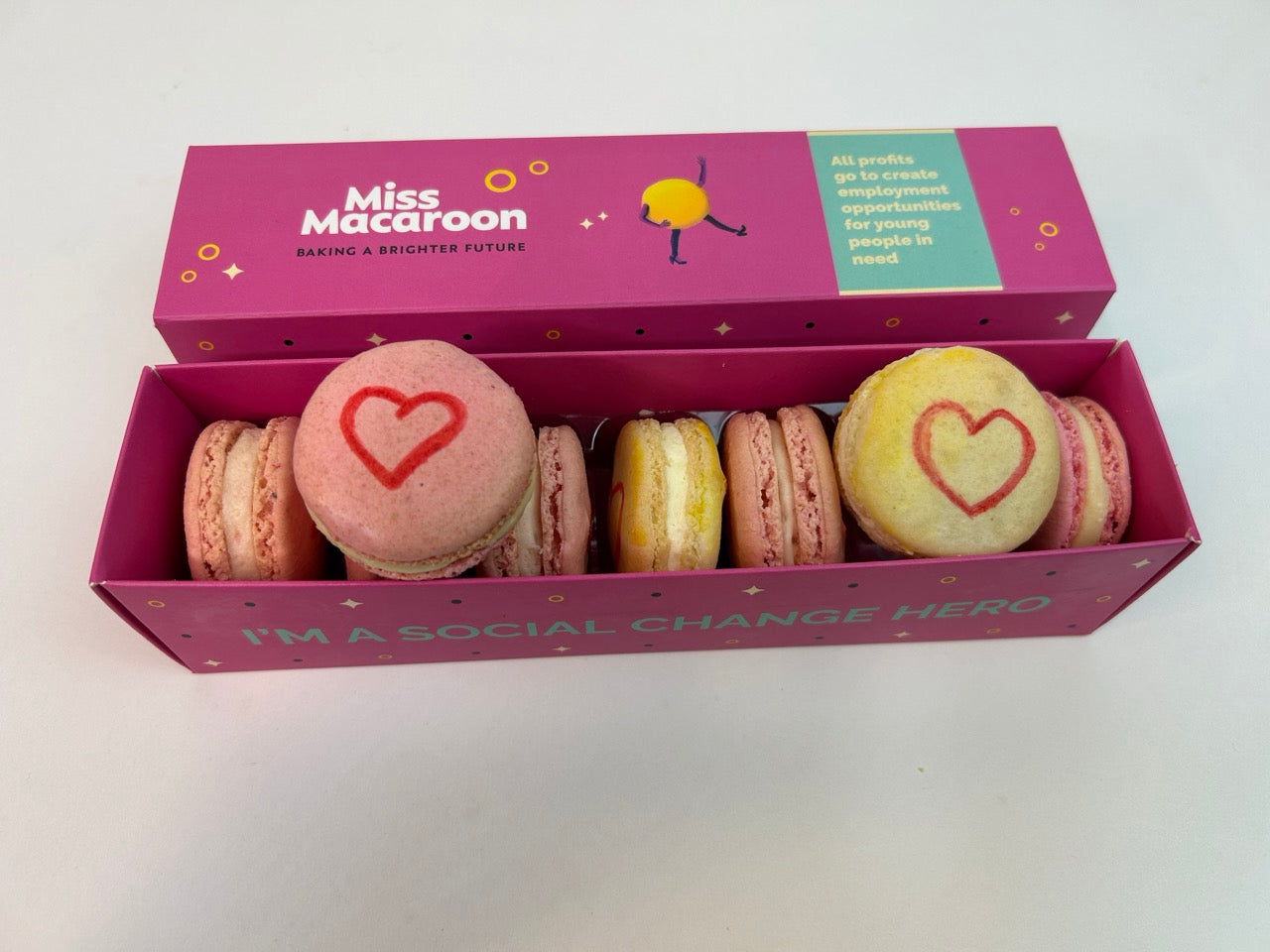 Pink gift box containing seven macaroons with a heart motif painted on, picture shows two hearts