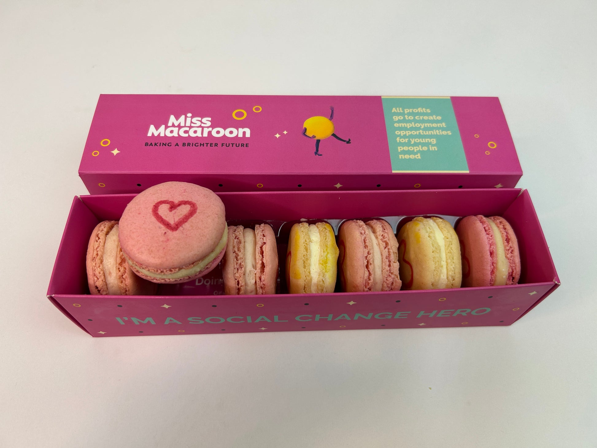 Pink gift box containing seven macaroons with a heart motif painted on.