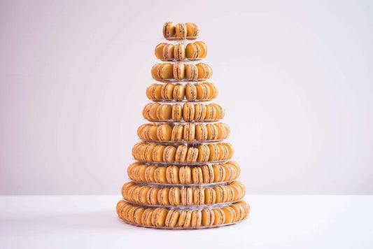 A tower of ten tiers is placed in the center. The background is a plain white and the macaroons are shades of yellow and orange.