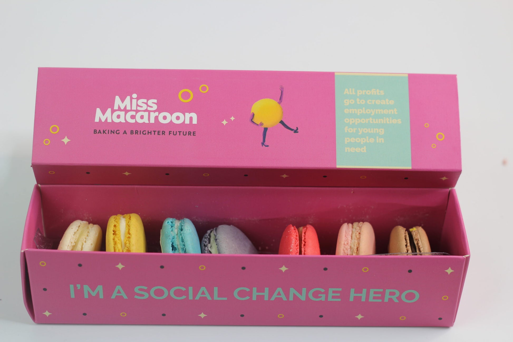 A pink box with multiple coloured macaroons is displayed. The box has 'I'm a social change hero' written.